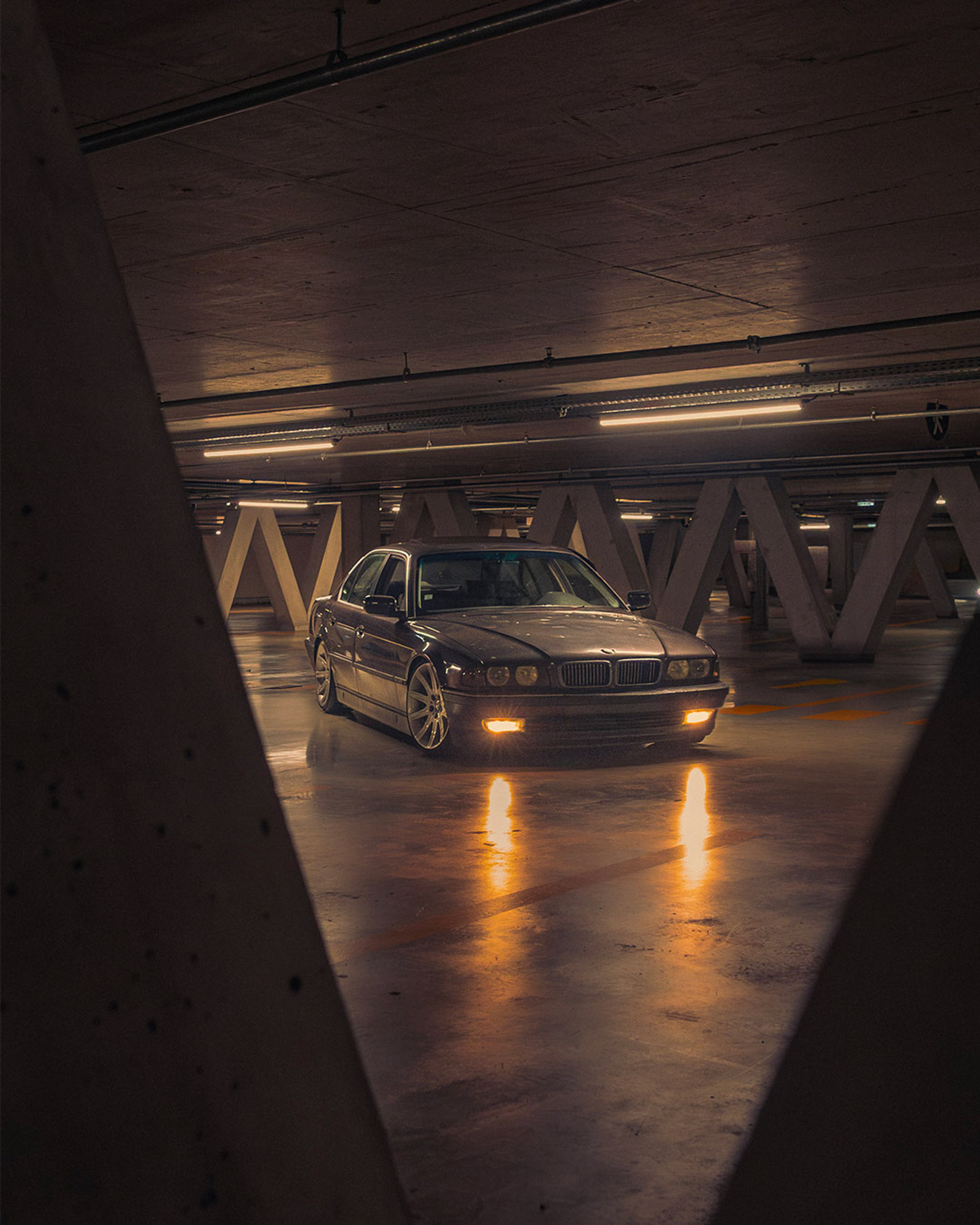 BMW Série 7 E38 735i vue de trois quarts avant dans un parking souterrain, phares antibrouillard allumés sur le sol humide
