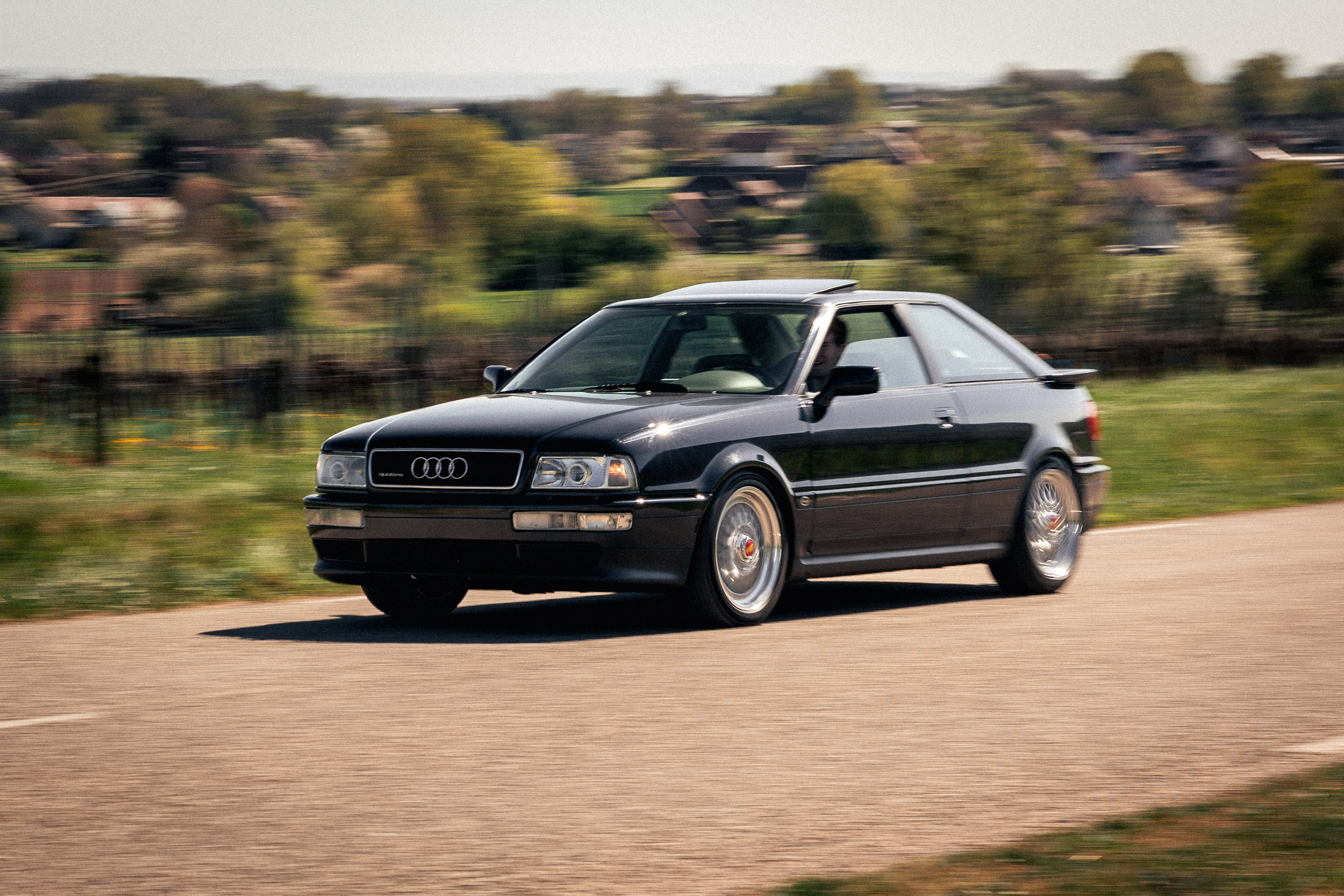 Audi Coupé quattro rouge garée devant un hangar en briques, lumière rasante de fin de journée
