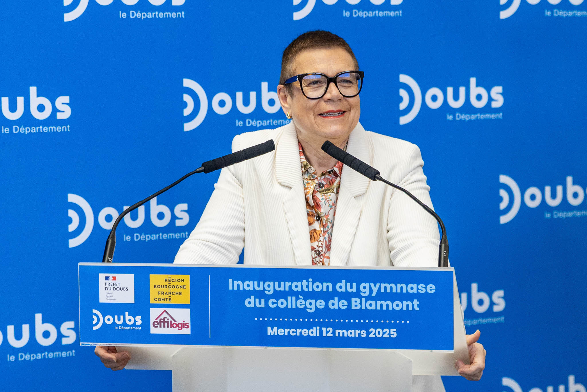 Prise de parole à un pupitre lors de l'inauguration du gymnase du collège de Blamont, fond bleu du Département du Doubs