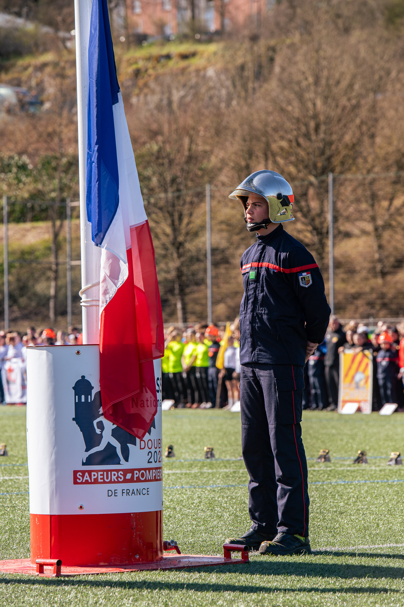 Sapeur-pompier en tenue debout près du mât du drapeau tricolore, finale du cross national des sapeurs-pompiers